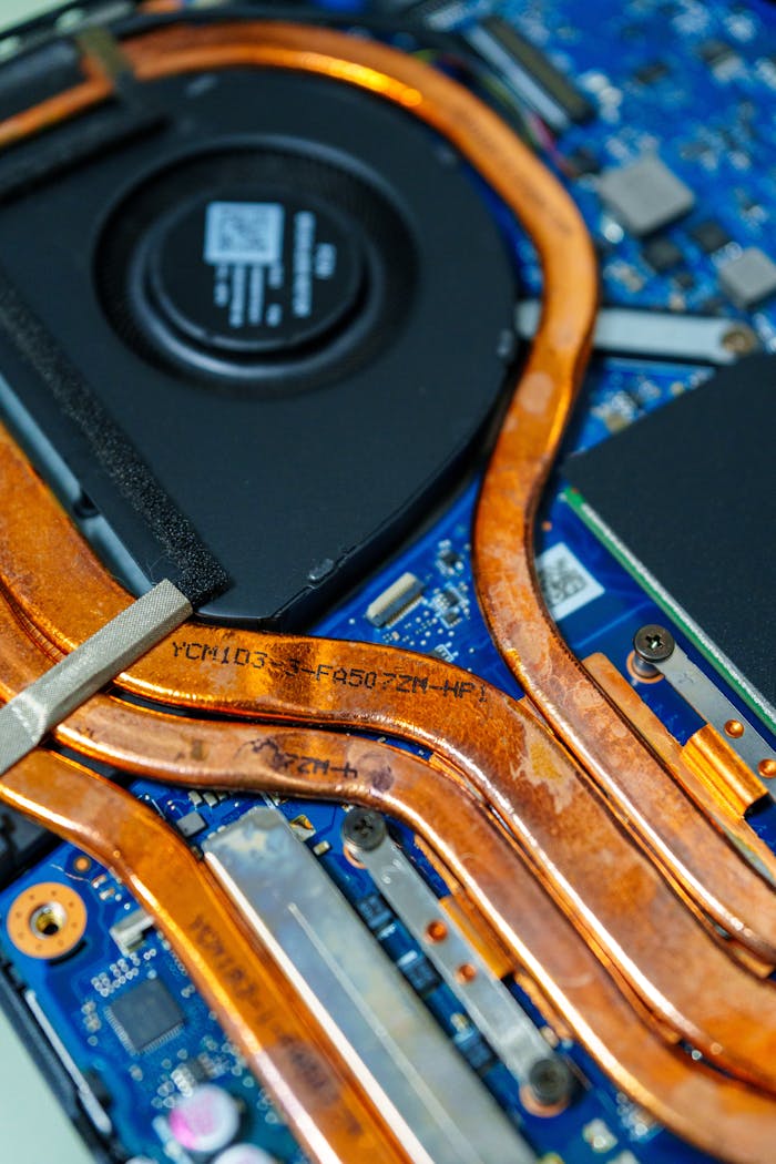 services-02 Detailed view of a laptop's cooling system showing copper heat pipes and intricate circuitry.