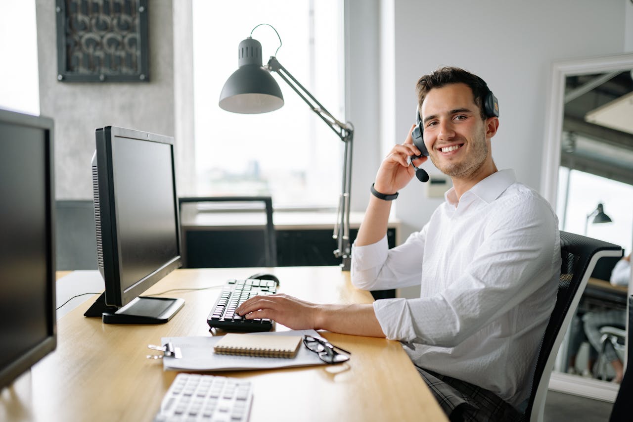 about-02 Smiling call center agent working at a desk with a headset and computer in a modern office.